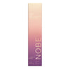 Korkea, suorakaiteen muotoinen NOBE Oat Wonder Luminous Lip Oil -pakkaus pystysuuntaisella väriliu'ulla vaaleasta beigestä yläosassa syvään violettiin alaosassa, kultaisensävyistä tekstiä läpi pakkauksen; pakkaus mattapintaista pahvia terävin reunoin; NOBE painettu pystysuunnassa groteskikirjasimella; etusivulla kauran kuvitusta ja tuotetietoja; ei ihmisiä tai käsiä näkyvissä; tausta yksinkertainen, studiokuva.