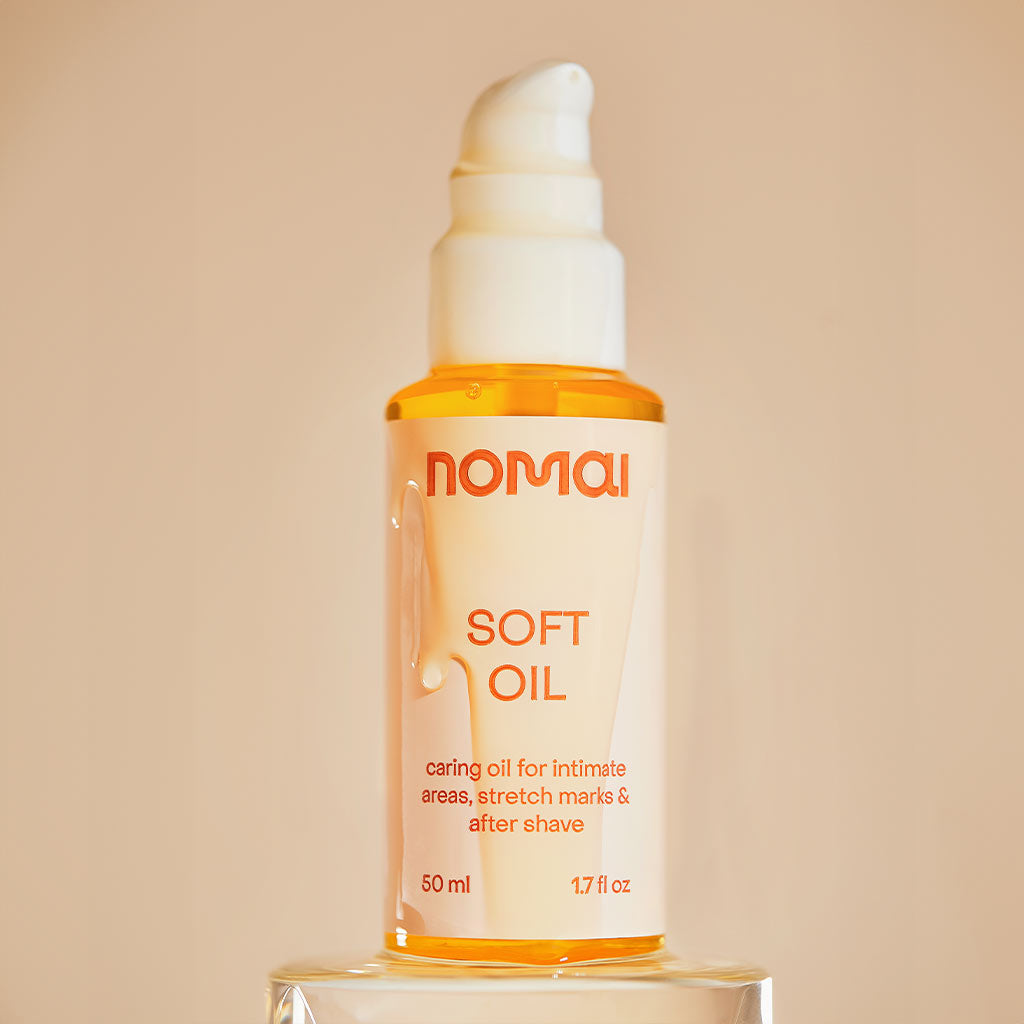 Nomai Soft OiI Intiimi- ja vartaloöljy; pullo Nomai Soft Oil -tuotetta oranssilla pumppuannostelijalla; pullo on valkoinen, mattapintainen ja sylinterinmuotoinen; etiketissä selkeä, yksinkertainen groteskikirjasin, jossa mainitaan käyttö intiimialueille, raskausarpiin ja parranajon jälkeiseen hoitoon sekä tilavuus "50 ml (1,7 fl oz)"; ei ihmisiä tai käsiä näkyvissä; studiotausta neutraali.