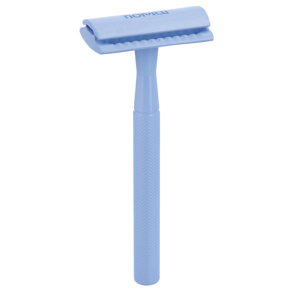 Nomai Superior Shaver; vaaleansininen uudelleenkäytettävä partaterä tekstuurisella kädensijalla, pystyssä valkoista taustaa vasten, ympäristöystävällinen vaihtoehto kertakäyttöisille partateröille; terä metallinen mattapinnalla, ei näkyvää etikettiä; kuvattu suoraviivaisena tuotekuvana ilman ihmisiä, pakkausta tai muuta rekvisiittaa.