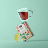 Nordqvist Lumoava Luomu Earl Grey; lasinen teekuppi tasapainoilee värikkään Earl Grey -teerasian päällä, vieressä limeviipale, pastellivihreää taustaa vasten; rasia suorakulmainen kirkkain monivärisin geometrisin kuvioin ja selkeällä lihavoidulla tekstillä ”Earl Grey”; teekuppi läpinäkyvä ja sylinterin muotoinen; mattapinta rasiassa; ei ihmisiä tai käsiä, studiotuotekuva.