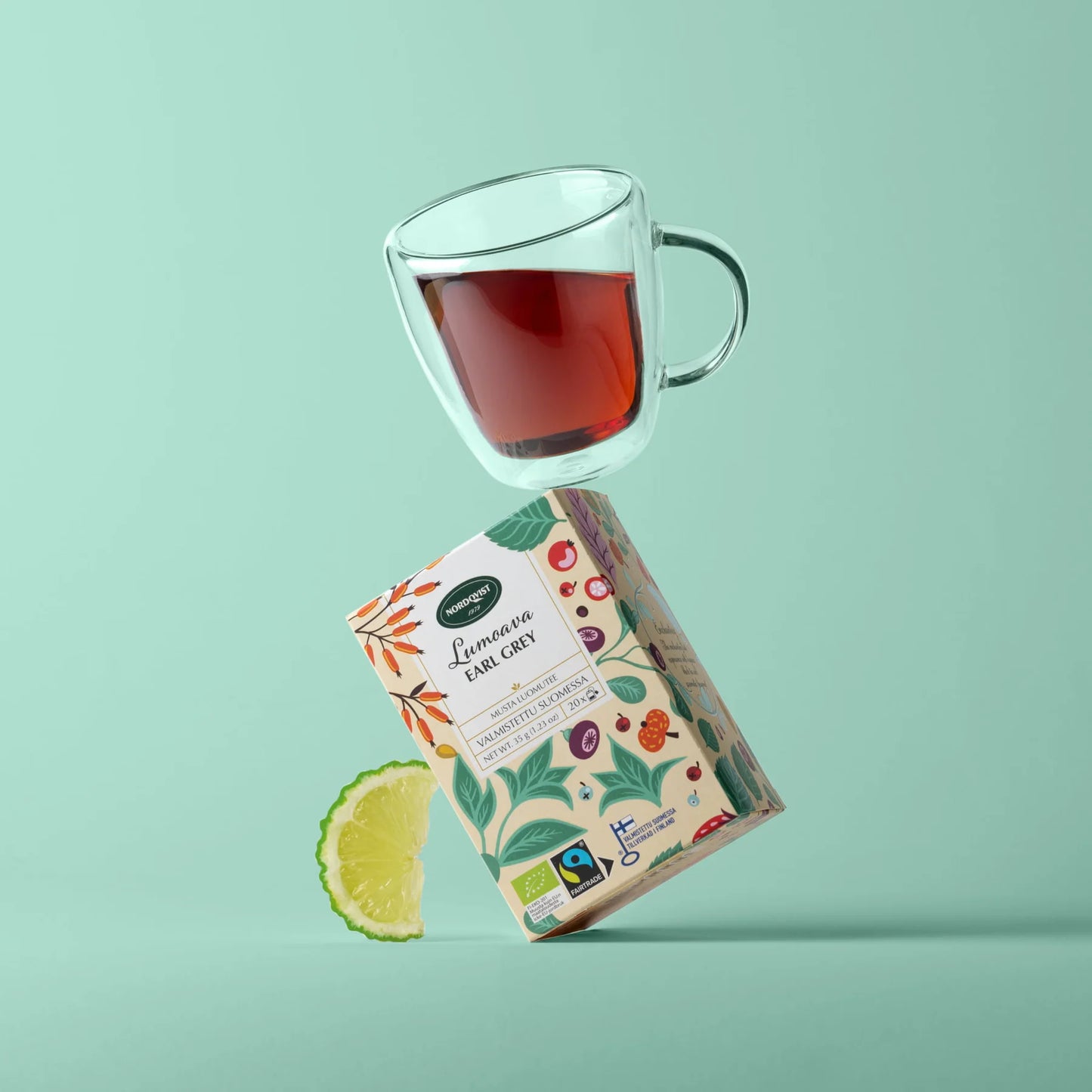 Nordqvist Lumoava Luomu Earl Grey; lasinen teekuppi tasapainoilee värikkään Earl Grey -teerasian päällä, vieressä limeviipale, pastellivihreää taustaa vasten; rasia suorakulmainen kirkkain monivärisin geometrisin kuvioin ja selkeällä lihavoidulla tekstillä ”Earl Grey”; teekuppi läpinäkyvä ja sylinterin muotoinen; mattapinta rasiassa; ei ihmisiä tai käsiä, studiotuotekuva.