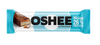 OSHEE Protein Bar Coconut & Caramel; OSHEE-runsasproteiininen patukka sinisessä ja valkoisessa pakkauksessa, merkitty ei sokeria, 26 % proteiinia ja kookos & karamelli; kääre matta lihavoidulla groteskikirjasimella; osittain avattu patukka vasemmalla näyttää vaalean täytteen ja karamellikerroksen; tausta valkoinen, ei ihmisiä tai käsiä; lähikuva, tuote keskitettynä.