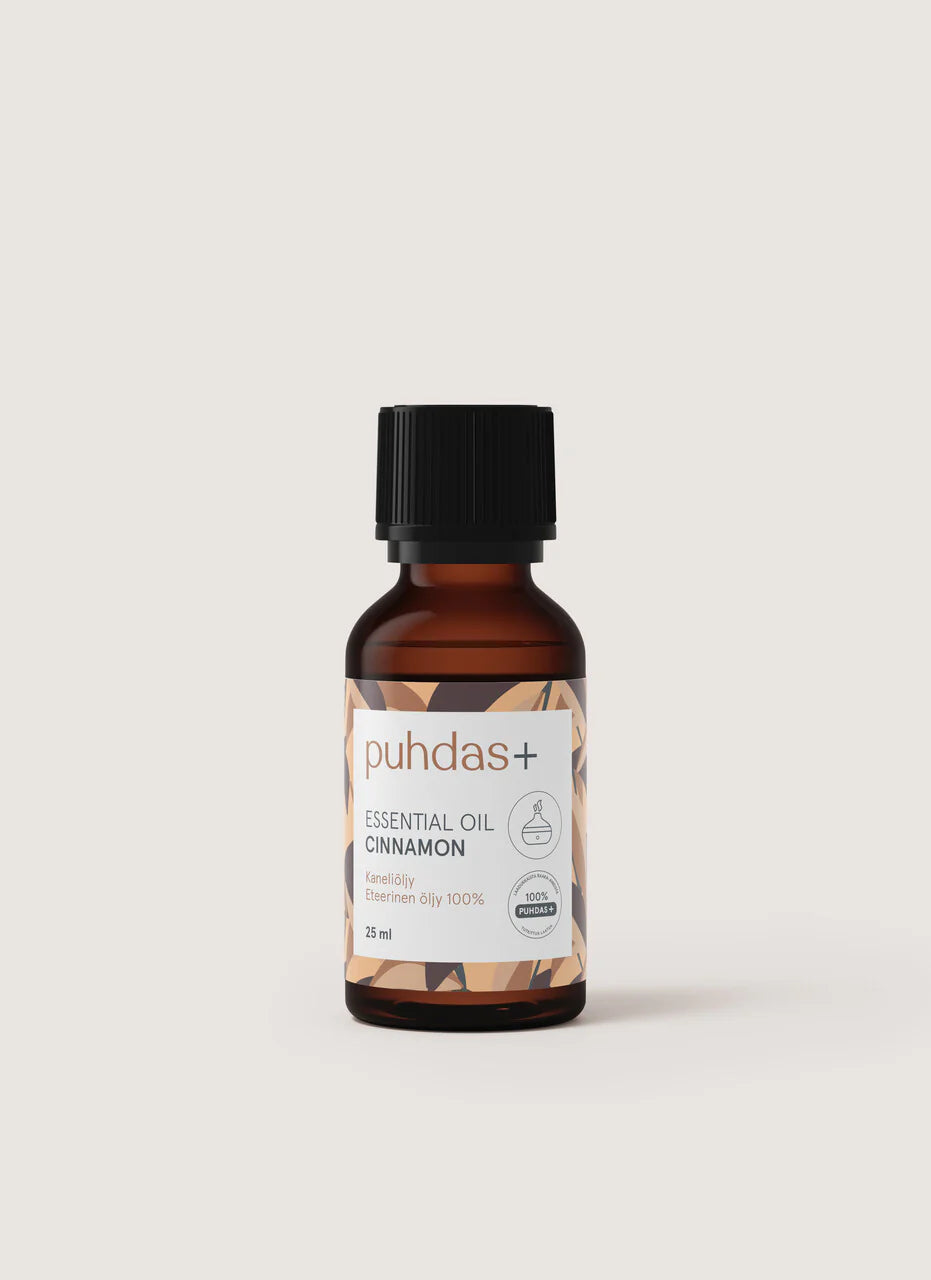 puhdas+ Essential Oil Cinnamon -pullo, pieni meripihkanvärinen lasipullo mattamustalla kierrekorkilla ja suorakulmaisella valkoisella etiketillä, pystyssä vaaleaa taustaa vasten; etiketissä lukee "puhdas+ Essential Oil Cinnamon" sekä englanniksi että suomeksi selkeällä tekstausvapaalla fontilla; ei ihmisiä tai toimintaa kuvassa.