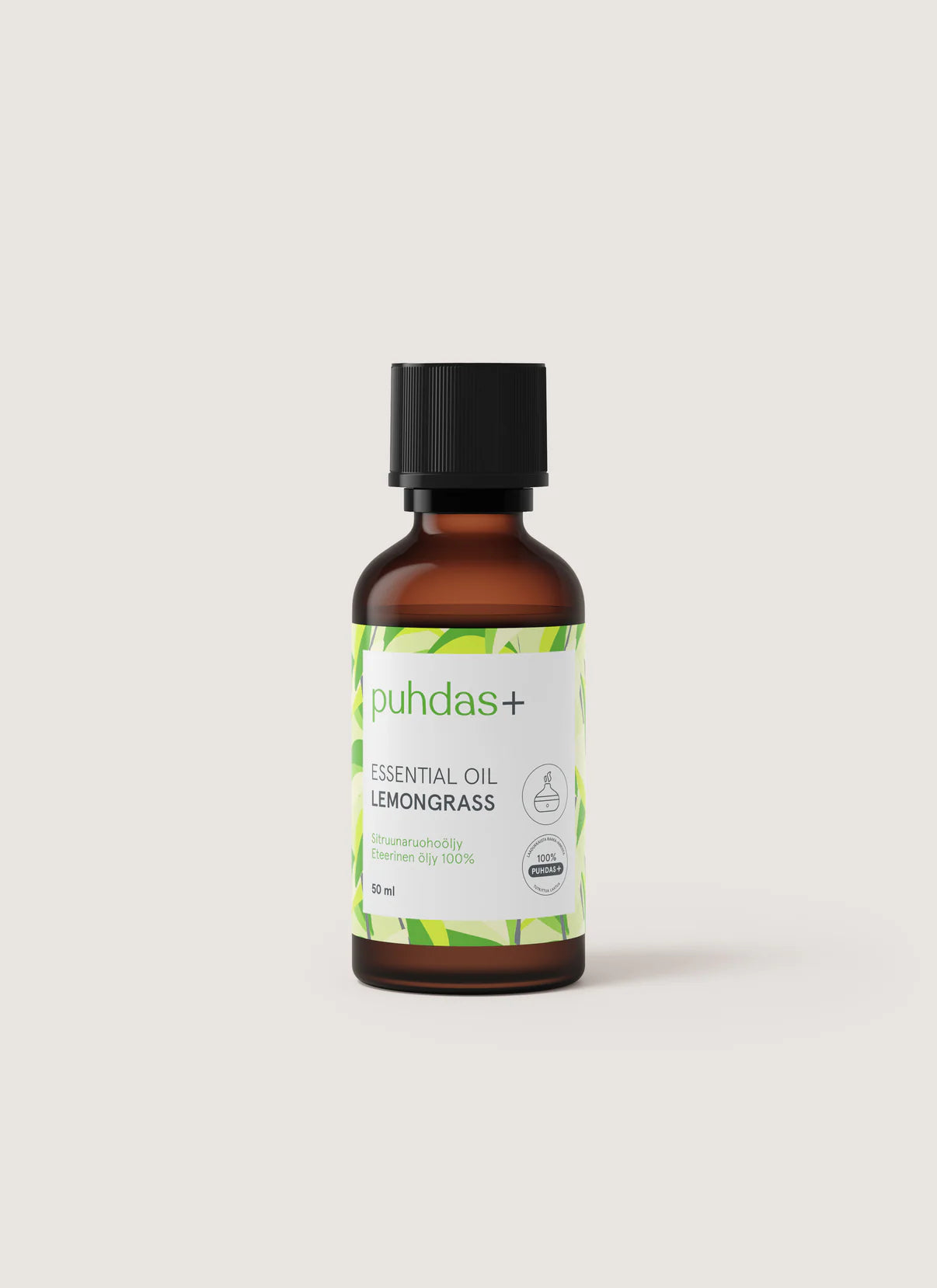 Puhdas+ Lemongrass Essential Oil -pullo, ruskea lasipullo mustalla muovisella kierrekorkilla ja suorakulmaisella vihreällä ja valkoisella etiketillä; pullo sylinterimäinen kiiltäväpinnalla; etiketissä "Puhdas+" modernilla tekstausvapaalla fontilla sekä "Lemongrass Essential Oil"; tuote kuvattu pystyssä tasaisella vaaleanbeigellä taustalla; ei ihmisiä tai käsiä näkyvissä.