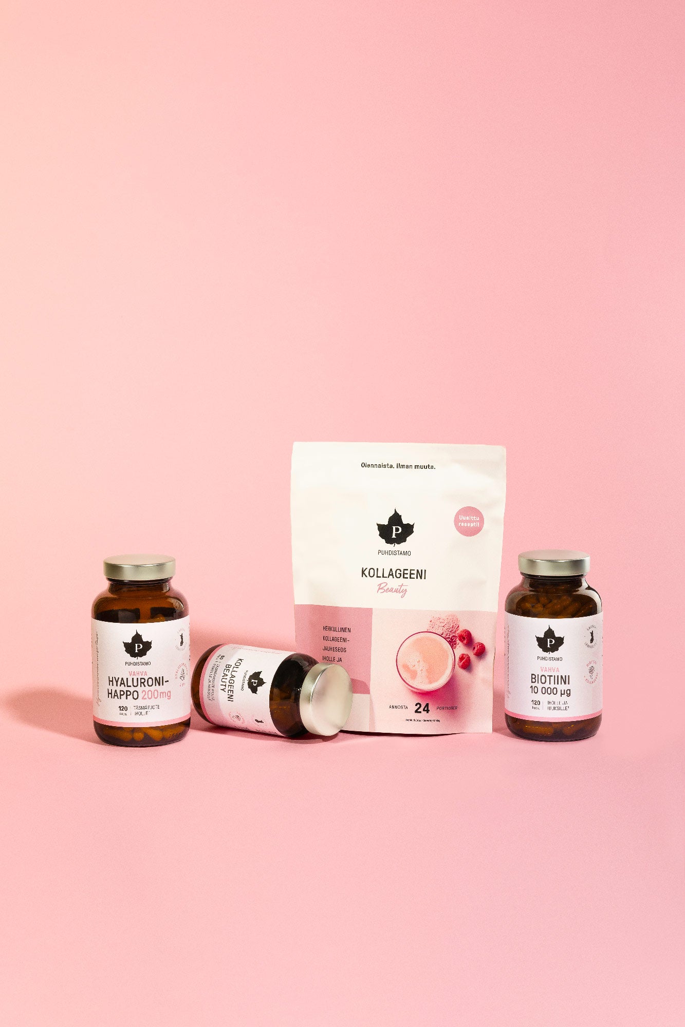 Puhdistamo Kollageeni Beauty; kolme pinkki-ruskeaa lisäravinnepulloa ja valkoinen pussi tekstillä Kollageeni esillä pinkillä alustalla pinkkiä taustaa vasten; pullot lieriömäisiä mattaetikettein ja yksinkertaisella groteskityypografialla; valkoisessa pussissa suurta lihavoitua tekstiä sekä smoothie- ja kollageeniheliksikuvituksia; ei ihmisiä tai käsiä; tasaisesti valaistu laaja tuotekuva.