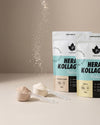 Puhdistamo Hera & Kollageeni Vanilja; kaksi Puhdistamo Herakollagen-proteiinijauhepussia, toinen vanilja- ja toinen cookies & cream -makuinen, edessä jauhetta täynnä olevat mittalusikat; kollageenipöly valuu yläreunasta alaosaan kuvassa; matat pussit uudelleensuljettavalla yläreunalla, tuotenimi ja maku lihavoidulla groteskilla; pussit pystyssä neutraalilla sileällä pinnalla, ei ihmisiä tai käsiä kuvassa.