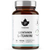A brown bottle labeled Puhdistamo Luontainen L-Teaniini with 60 capsules, each containing 100 mg, and text in Finnish. The plastic container has a matte finish and a black screw cap. The white label shows bold, sans-serif black lettering, a stylized leaf logo above the product name, and two green quality/vegan icons. The photo is shot against a plain light background; no other objects or hands are visible.
