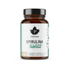 Puhdistamo Spirulinatabletit -pullo, ruskea lasi, musta muovikorkki, kiiltäväpinta; valkoinen mattaetiketti vihreällä ja mustalla groteskitekstillä, tyylitelty lehtilogo, spirulinapitoisuus suomeksi