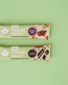 Kaksi Puhdas Snack -patukkaa vaaleanvihreällä taustalla; ylempi patukka merkitty karpalo-goji, alempi kaakao; molemmat pakattu suorakaiteen muotoisiin, mattapintaisiin ja värikkäisiin muovikääreisiin, joissa on painettuna karpaloiden, goji-marjojen tai kaakaopapujen kuvia; tuotenimi ja maku lihavoidulla groteskitekstillä; ei ihmisiä tai käsiä näkyvissä.