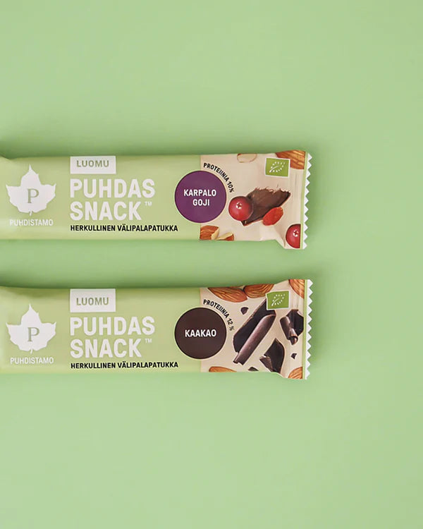 Kaksi Puhdas Snack -proteiinipatukkaa vaaleanvihreällä taustalla; toinen merkitty karpalo-goji, toinen kaakao; suorakaiteen muotoiset patukat mattapintaisissa muovikääreissä, toisessa kääreessä punaisia marjoja ja gojia, toisessa kaakaopapuja; lihavoitu groteskituotenimi painettu pystysuunnassa molempiin pakkauksiin; ei ihmisiä tai käsiä näkyvissä kuvassa; molemmissa kääreissä kuvia niiden terveellisistä pääraaka-aineista.