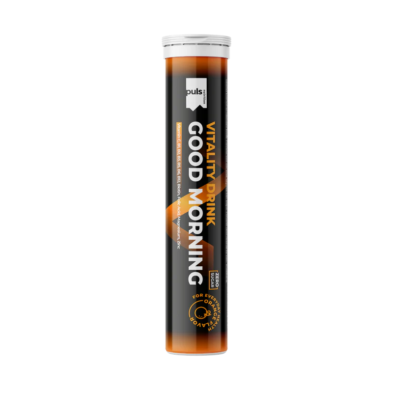 Puls Good Morning poretabletti: sylinterimäinen putkilo tekstillä "Vitality Drink GOOD MORNING" oranssi-mustalla designilla, puls-brändäys ja lupaus energisoivasta juomasta fyysisen ja henkisen vireyden tueksi; pakkaus vaikuttaa metallilta tai muovilta kiiltäväpinnalla; teksti on lihavoitua groteskikirjasinta; pääväreinä oranssi, musta ja valkoinen; tuote seisoo pystyssä neutraalia taustaa vasten studiokuvassa, ei ihmisiä tai käsiä näkyvissä.