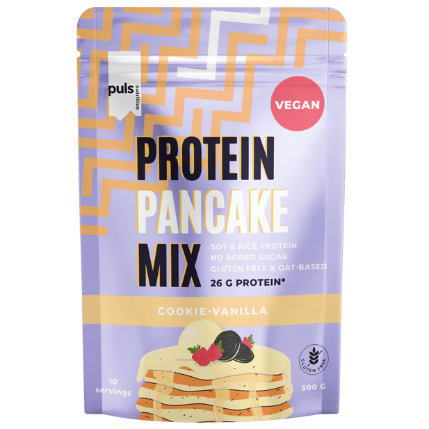 Puls Pancake Mix Cookie-Vanilja; vegaaninen proteiinipannukakkujauhepussi, cookie-vanilja-maku; pakkaus violetti keltaisin sävyin, pinta matta; etiketissä kuva pinosta pannukakkuja kerman ja keksin kera; lihavoitu groteskiteksti kertoo lisätyn sokerin puuttumisesta, 26 g kasviproteiinia ja gluteenittomuudesta; valkoinen studiotausta, tuote keskellä, ei ihmisiä tai muita esineitä.