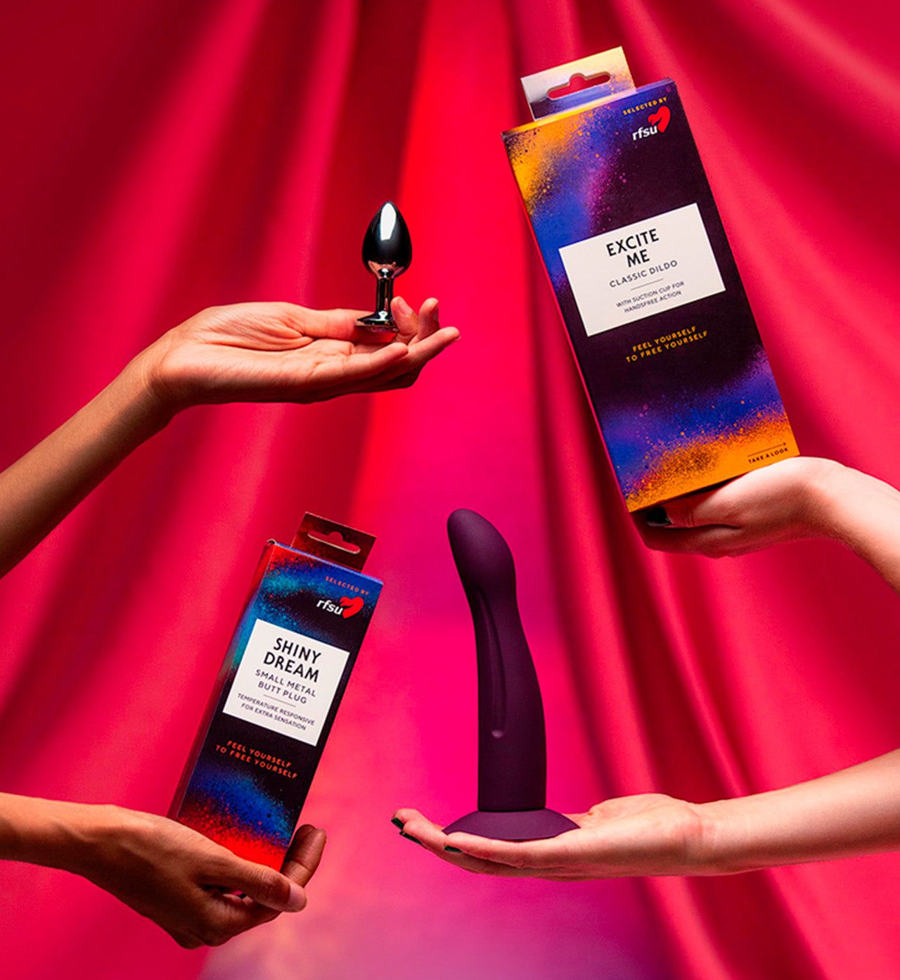 Three hands hold sex toys and colorful packaging against a bright pink fabric background, featuring a black butt plug with a matte finish, a glossy purple dildo with a curved shape, and two rectangular product boxes. One box is labeled Shiny Dream and the other Excite Me vibrator in bold sans-serif font style. The shot is close up, showing details of the objects and hands only.