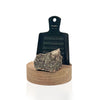 Rivsalt Walnut Suolaraastin; metallinen raastin tekstillä rivsalt seisoo pystyssä pyöreällä puisella alustalla, edessä suuri pala kivisuolaa; ruostumattomasta teräksestä valmistettu raastin harjatulla pinnalla, suorakaiteen muotoinen pyöristetyin reunoin; teksti rivsalt painettu vaakasuunnassa minimalistisella groteskifontilla; pyöreä alusta vaaleaa puuta; ei pakkausta näkyvissä; tausta valkoinen, tuote keskitetty, ei ihmisiä kuvassa.