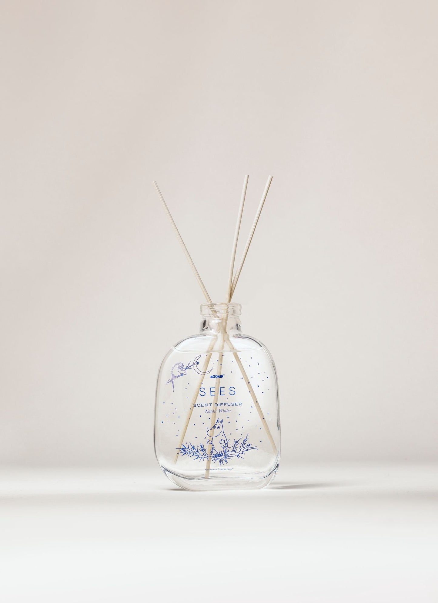 SEES x Moomin Room Diffuser Nordic Winter; kirkas lasinen tuoksudiffuusoripullo vaalein puutikuin ja hienovaraisin sinisin kasvikuvioin seisoo pystyssä neutraalia taustaa vasten; pullo lieriömäinen ja kiiltävä, valmistettu läpinäkyvästä lasista; ohuita, suoria tikkuja ulottuu aukosta; ei etikettiä tai tekstiä pinnalla; tausta tasaisesti valaistu ilman rekvisiittaa tai ihmisiä kuvassa.
