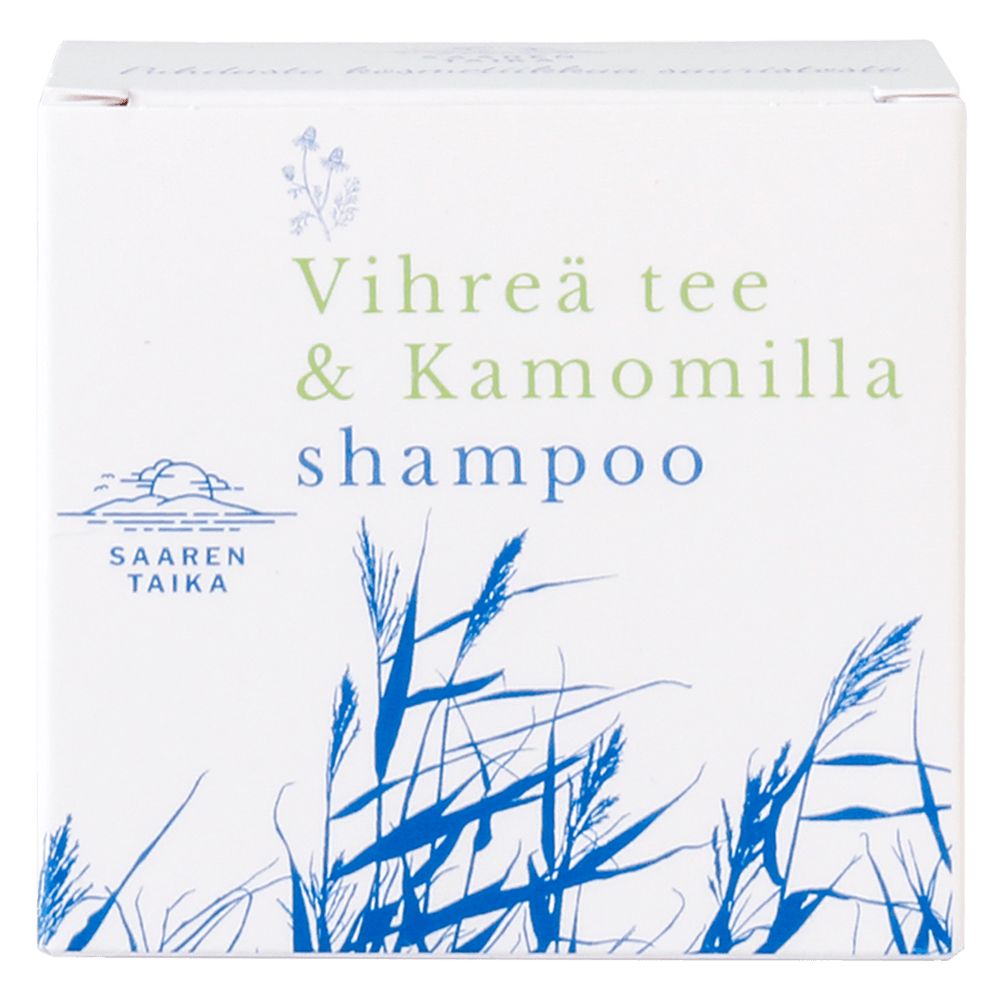 A white box with blue and green text reading Vihreä tee & Kamomilla shampoo features blue illustrations of grass and the Saaren Taika logo on the packaging. The box is rectangular with a matte finish. Product name uses bold sans-serif fonts in multiple colors. Packaging is shown against a plain, light background in a straight-on shot. No people or hands are present.