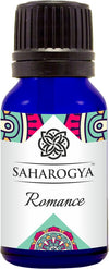 A blue glass bottle labeled SAHAROGYA Romance, featuring an elegant, colorful pattern on the label and a black screw cap. Cylindrical shape with glossy finish. Label includes serif and sans-serif fonts in white and gold against a multicolored background. No people or hands visible. Shot against a plain white background, centered product view.