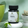 Saharogya Neem 750 mg; pullo tekstillä ”Saharogya Neem” valkoisella korokkeella neem-lehden vieressä, taustalla vihreä kulho ja lautanen tabletteja; etiketissä ilmoitettu 60 tablettia valmistettuna 100 % luonnonmukaisista yrteistä ja luonnollisista ainesosista; pullo lieriömäinen, vaikuttaa mattavalkoiselta vihrein etikettitehostein; tausta pelkistetty, ei ihmisiä tai käsiä näkyvissä.