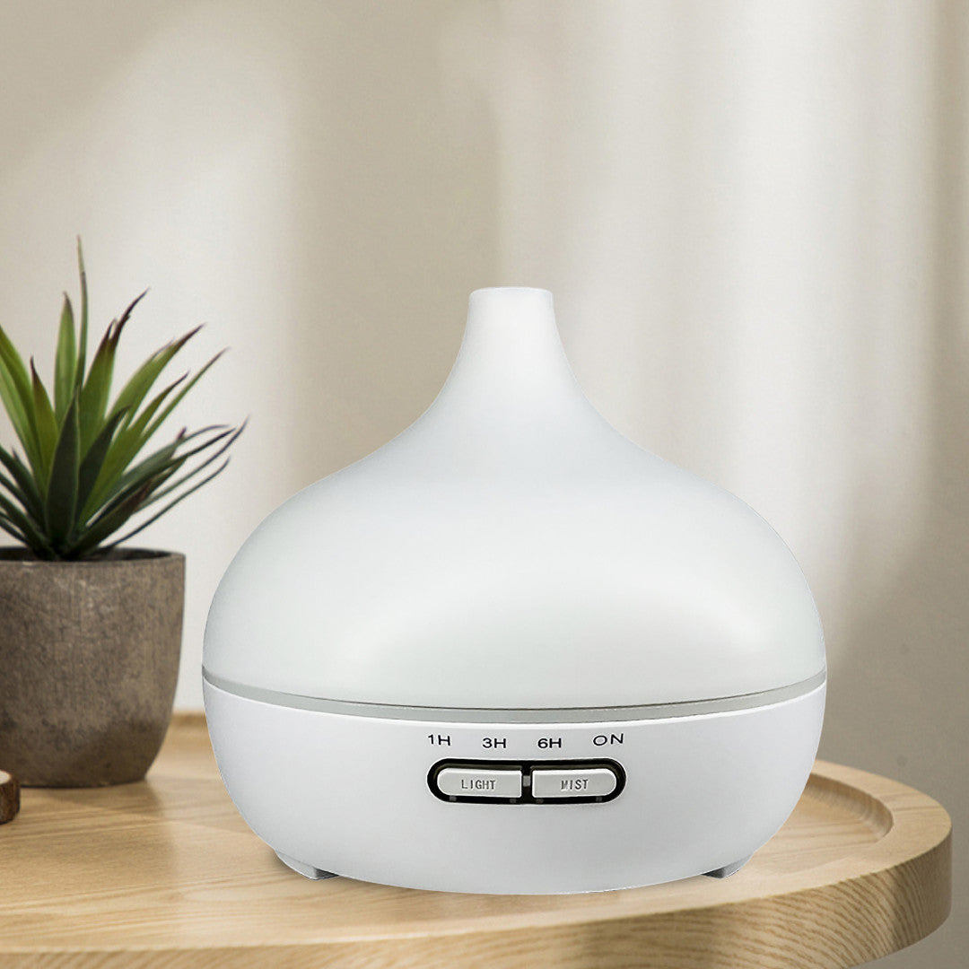 Salt Aroom Suola-Aroma Diffuuseri Aava; valkoinen eteerisen öljyn diffuusori ajastinpainikkeilla seisoo mattapintaisella puupöydällä pienen ruukkukasvin vieressä; diffuusori on sylinterinmuotoinen pyöristetyin reunoin, ajastimen säätimet selkeällä groteskitekstillä; pehmeä luonnonvalo suodattuu neutraalinvärisistä verhoista taustalla; ei ihmisiä, käsiä tai pakkausta näkyvissä.