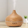 Salt Aroom Suola-Aroma Diffuuseri Aava; puukuvioitu ultraäänidiffuusori päästää höyryä vaalealla pöydällä; diffuusori on pyöreä, mattapintainen, ilman näkyvää merkkiä tai etikettiä; pieni vihreä ruukkukasvi diffuusorin takana, beige seinä taustalla; ei ihmisiä, käsiä tai pakkausta näkyvissä tässä tuotekuvassa.