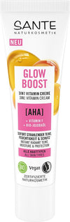 Sante Glow Boost 3 in 1 Vitamiinivoide; tuubi 3-in-1-vitamiinivoidetta AHA-hapolla, F-vitamiinilla ja luomu-jojobaöljyllä; pakkaus korostaa välitöntä hehkua, kosteutusta, vegaanisia ainesosia ja sertifioitua luonnonkosmetiikkaa; tuubi seisoo pystyssä mattapinnalla, esittäen luettavaa painettua tekstiä valkoisena ja oranssina vaaleanpunaista taustaa vasten; ei ihmisiä tai käsiä näkyvissä; tuote yksin valkoisella pinnalla lähikuvassa.