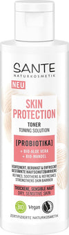 Sante Skin Protection Kasvovesi; valkoinen sylinterinmuotoinen pullo merkitty Sante Naturkosmetik Skin Protection Toner seisoo pystyssä; pinta mattapintainen, teksti painettu selkeällä groteskikirjasimella; etiketissä vegaani- ja luomusertifiointimerkinnät; pullossa mainitaan probiootti, luomu-aaloe vera ja luomu-manteli kuivalle tai herkälle iholle; kuvan tausta yksivärinen.