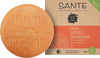 Sante Suihkugeelipala Happiness; pyöreä oranssi saippuapala kohokuvioidulla tekstillä CARE FOR YOU AND THE WORLD, Sante Naturkosmetik -laatikon vieressä merkinnällä Feste Happiness Duschpflege ja appelsiiniviipalekuvituksella; laatikko korostaa vegaani- ja luomusertifiointia; saippua on mattapintainen, pyöreä ja yksivärinen; pakkaus on suorakulmaista pahvia painetulla designilla ja groteskikirjasimella; tausta valkoinen, tuotekuva ilman muita elementtejä.