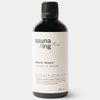 sauna/ing Sauna Scent Juniper & Spruce; musta lieriömäinen pullo mattapinnalla ja mustalla kierrekannella; valkoinen suorakaiteen muotoinen etiketti etuosassa mustalla groteskitekstillä Sauna Scent: Juniper & Spruce from Sauna Ing Finland; pienempi teksti listaa katajan ja kuusen ainesosina, numeeriset koordinaatit ja 100 ml; valkoinen tausta, ei ihmisiä tai muita esineitä kuvassa.