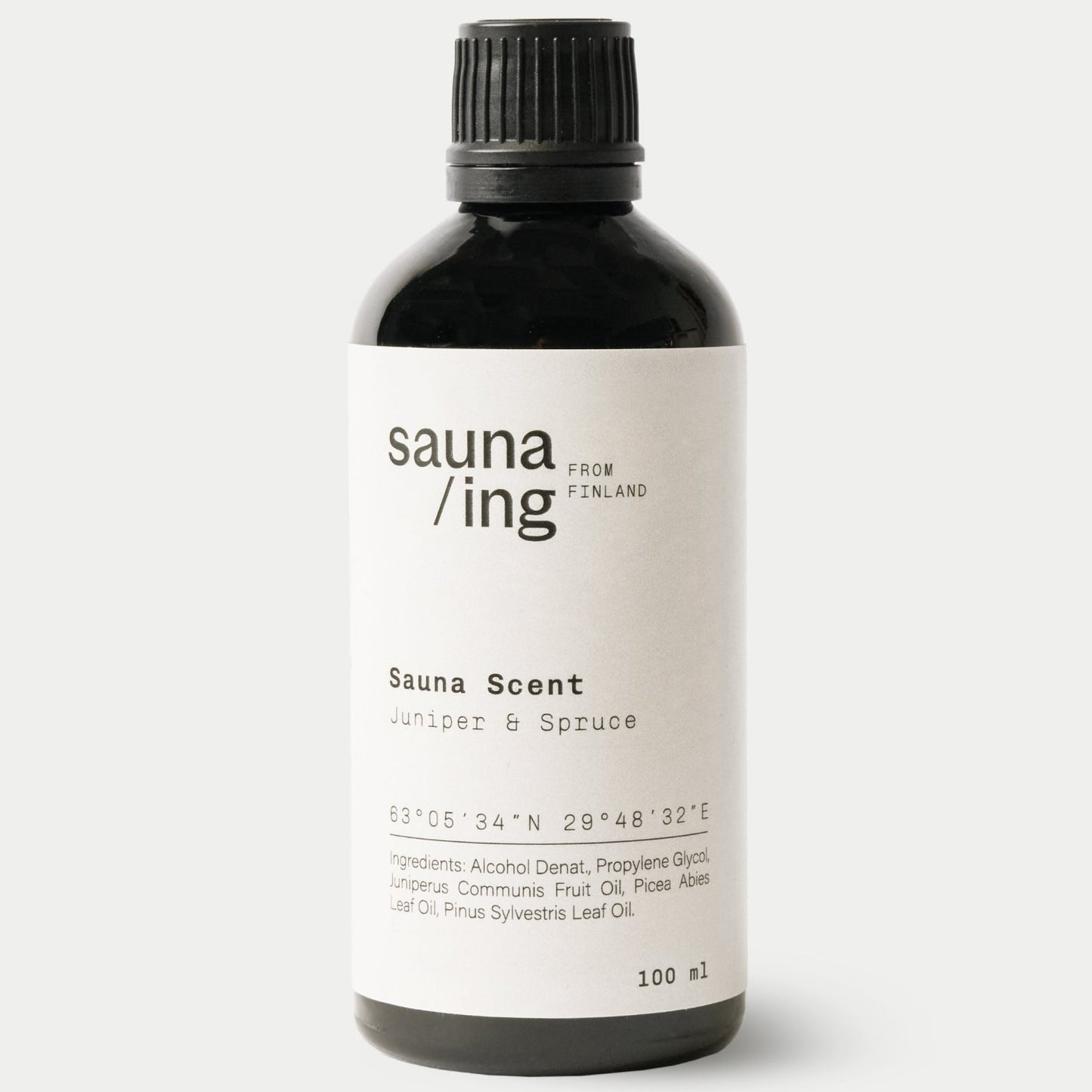 sauna/ing Sauna Scent Juniper & Spruce; musta lieriömäinen pullo mattapinnalla ja mustalla kierrekannella; valkoinen suorakaiteen muotoinen etiketti etuosassa mustalla groteskitekstillä Sauna Scent: Juniper & Spruce from Sauna Ing Finland; pienempi teksti listaa katajan ja kuusen ainesosina, numeeriset koordinaatit ja 100 ml; valkoinen tausta, ei ihmisiä tai muita esineitä kuvassa.