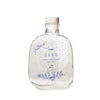 SEES x Moomin Room Diffuser Nordic Winter; kirkas lasipullo puisella korkilla, tekstillä MOOMIN SEES SCENT DIFFUSER Nordic Winter; lieriömäinen muoto, sileä kiiltäväpinta; etiketissä sinistä isokokoista groteskitekstiä ja yksinkertainen sininen kuvitus muumihahmosta, talvisia oksia ja pieniä pisteitä; ei ihmisiä tai käsiä; neutraali yksinkertainen tausta; tuote keskitettynä kuvaan.