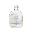 SEES x Moomin Room Diffuser Nordic Winter; kirkas lasipullo puisella korkilla, tekstillä MOOMIN SEES SCENT DIFFUSER Nordic Winter; lieriömäinen muoto, sileä kiiltäväpinta; etiketissä sinistä isokokoista groteskitekstiä ja yksinkertainen sininen kuvitus muumihahmosta, talvisia oksia ja pieniä pisteitä; ei ihmisiä tai käsiä; neutraali yksinkertainen tausta; tuote keskitettynä kuvaan.