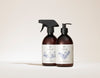 SEES x Moomin Dish Wash Spray; kaksi ruskeaa pulloa valkoisin etikettein ja mustin pumpuin, toisessa suihkesuutin ja toisessa työntöannostelija, merkitty SEES ja koristeltu minimalistisin viivapiirroksin, kasvikuvituksin ja luonnollisen tyylikkyyden tuntua vaaleaa taustaa vasten; molemmissa pulloissa lieriömäinen lasirunko mattapinnalla; etiketit valkoisia yksinkertaisin mustin groteskitekstein; asetelma tasaisesti valaistu, näyttää vain tuotteet ilman ihmisiä tai käsiä.