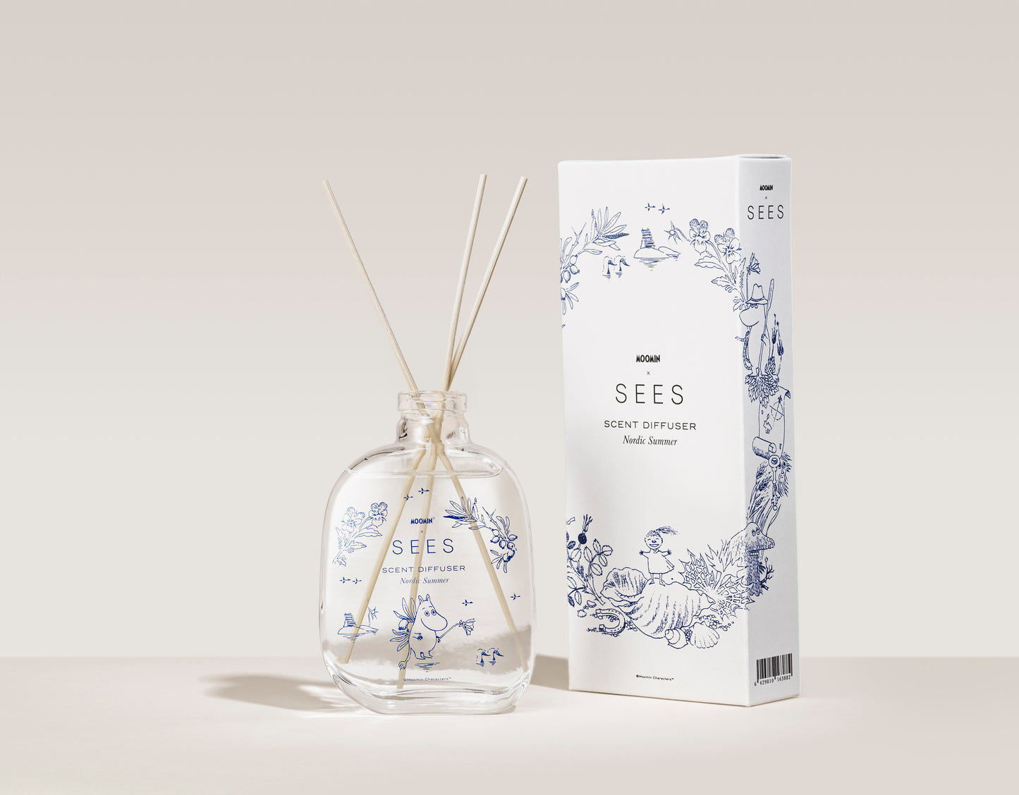 SEES x Moomin Room Diffuser Nordic Summer; kirkas lasinen tuoksudiffuusori kolmella vaalealla puutikulla pystyssä; aseteltuna mattavalkoisen suorakaiteen muotoisen pakkauksen viereen, jossa sinisiä kasvikuvituksia ja mustaa groteskitekstiä SEES Scent Diffuser Nordic Summer; molemmat esineet vaalealla, yksinkertaisella taustalla; ei ihmisiä tai käsiä kuvassa.
