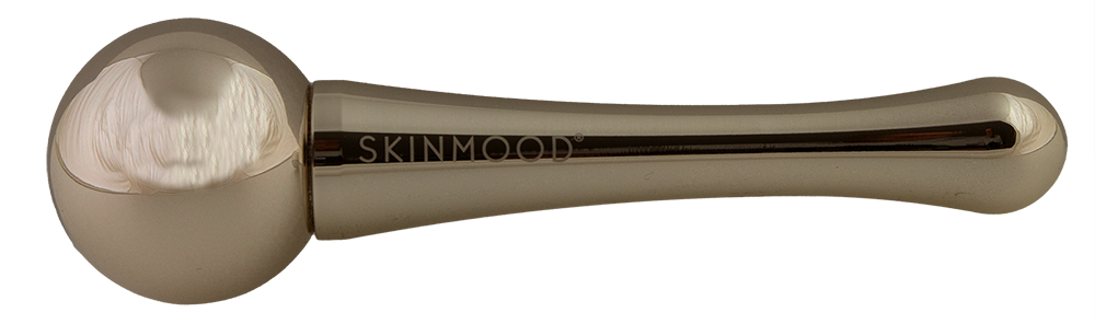 Metallinen SKINMOOD-kasvohierontatyökalu pyöreällä, sileällä päällä ja asteittain kapenevalla kahvalla, viimeistelty kiiltävän hopeisena; brändinimi SKINMOOD painettu selkeästi kahvaan isoin groteskikirjaimin; ei pakkausta tai muita esineitä näkyvissä; työkalu lepää puhtaalla, yhtenäisellä valkoisella taustalla ilman ihmisiä tai toimintaa.