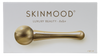 Kultainen kasvorulla, jossa merkintä SKINMOOD ja teksti Luxury Beauty - Roller, esiteltynä tyylikkäästi valkoisella pakkauksella, sopii kohottamaan ihonhoitorutiinia; kultainen lieriömäinen rullatyökalu metallisella viimeistelyllä; kahvassa selkeä musta groteskiteksti SKINMOOD ja Luxury Beauty - Roller; rullassa pyöristetyt päät; valkoinen suorakaiteen muotoinen rasiatausta, ei ihmisiä tai käsiä; studiovalaistus tasaisella pinnalla.