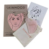 SkinMood Gua Sha Beauty Tool Hierontalasta; SKINMOOD Gua Sha -settikokonaisuus, jossa pinkki sileä ja litteä kasvojenhierontatyökalu pyöristetyin reunoin, kermanvärinen kangaspussi narusuljennalla sekä käyttöohjekortti viivapiirroksin kasvokuviosta; kaikki aseteltuna suorakulmaisen pakkauksen sisään tai eteen kuvitetulla kasvoaiheella ja tuotetiedoin; asetelma tyylikkäästi valkoisella taustalla.