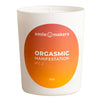 A white candle with an orange label reading smile makers ORGASMIC MANIFESTATION of Hot. The label features a gradient background. The candle is cylindrical with a matte finish, and the orange label wraps around its body vertically. Text is in bold uppercase sans-serif font. The product stands alone against a neutral background in a front-facing studio shot. No people or other objects are visible in the image.