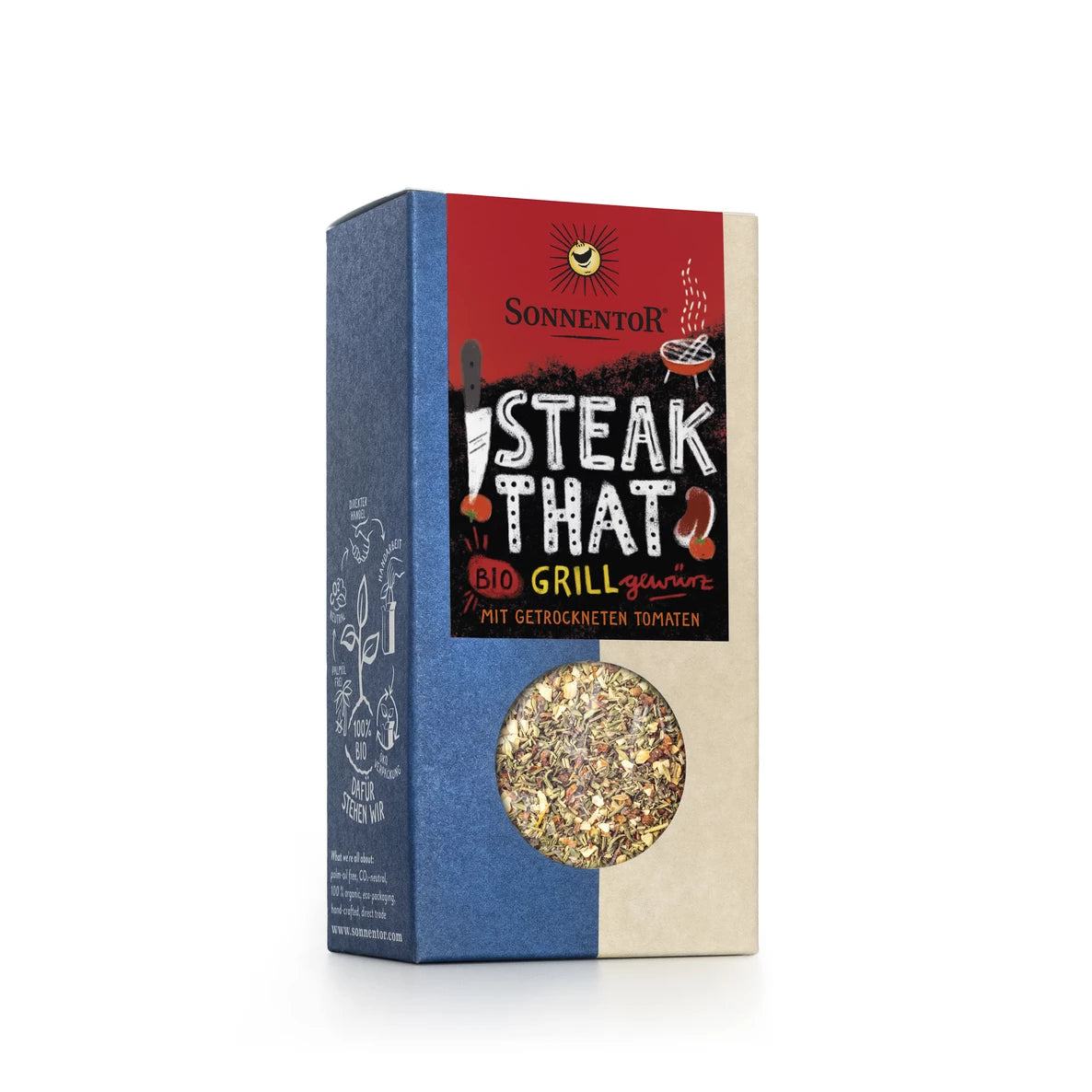 Laatikko Sonnentor Steak That -luomugrillimaustetta kuivatuin tomaatein. Suorakulmainen pahvilaatikko mattapinnalla; päävärit sininen, beige ja punainen. Etupuolella on grilliaiheista grafiikkaa ja kirkas ikkuna paljastaa sekoitetut mausteet sisällä. Tuotenimi on luettavissa etupuolella. Ihmisiä tai käsiä ei näy, pelkistetty tausta, studiotuotekuva.