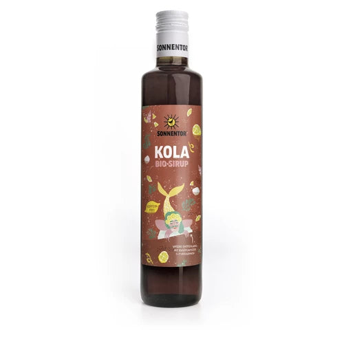 Ruskea lasipullo Sonnentor Kola Bio-Sirup -siirappia valkoisella korkilla ja värikkäällä etiketillä, jossa on leikkisiä kuvituksia merenneidosta, erilaisista hedelmistä, kuplista ja kola-ainesosista. Pullo on lieriömäinen sileäpintainen ja kiiltäväpintainen. Etiketissä käytetään sekalaista pääteviivatonta fonttia useissa kirkkaissa väreissä. Tausta on pelkistetty ja siisti. Ihmisiä tai käsiä ei näy kuvassa.