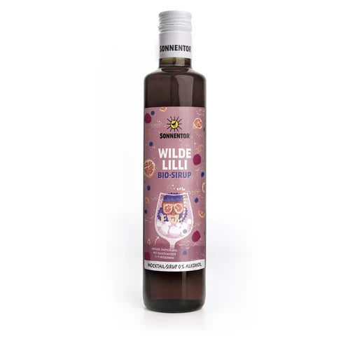 Pullo Sonnentor Wilde Lilli Bio-Sirup -siirappia eloisalla violetilla etiketillä, jossa on värikkäitä hedelmäkuvituksia ja tyylitelty juomalasi. Pullo on pystyssä, lieriömäinen, valmistettu tummasta lasista kiiltäväpinnalla. Etiketissä on lihavoitua valkoista tekstiä tuotenimelle. Ihmisiä tai käsiä ei näy. Pelkistetty valkoinen tausta; edestä otettu tuotekuva.