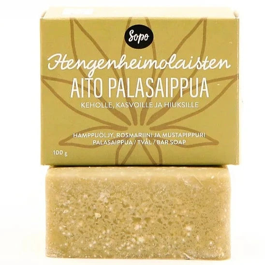 Sopo Hengenheimolaisten Aito Palasaippua; vihertävä saippuapala sen pahvipakkauksen edessä suomenkielisellä tekstillä hamppuöljystä, rosmariinista ja mustapippurista; saippua suorakulmainen sileine reunoineen ja mattapinnalla; ruskeassa pahvilaatikossa painettu lehtimotiivi ja lohkomainen typografia; tausta yksinkertainen, ei ihmisiä eikä käsiä näkyvissä.