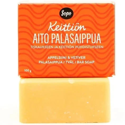 Sopo Keittiön Aito Palasaippua; oranssi suorakaiteen muotoinen pahvilaatikko mattapinnalla valkoisin ja keltaisin suomenkielisin tekstein seisoo kiinteän keltaisen suorakaiteen muotoisen saippuapalan päällä; saippuan pinta pakkauksesta poistettu ja sileä; etiketissä luettavissa maininnat "appelsiini" ja "vetiveri"; ei ihmisiä eikä käsiä näkyvissä, tausta neutraali, tuote keskitetty kuvaan.
