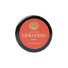 Sopo Sävyttävä Metsäbiomi Huulivoide & Poskipuna; pyöreä rasia tekstillä "Sopo Soft Coral Lip & Cheek Balm with Forest Biome", korallinvärinen kansi ja valkoista groteskitekstiä; rasian pohja mattapintainen ja luonnonvalkoinen; ei muita kuvioita tai koristeellisia yksityiskohtia näkyvissä; tausta valkoinen; kuvassa vain tuote, ei ihmisiä eikä käsiä näkyvissä.