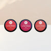 Sopo Sävyttävä Metsäbiomi Huulivoide & Poskipuna; kolme pyöreää Sopo Lip & Cheek Balm -rasiaa sävyissä Foxy Red, Wild Raspberry ja Soft Coral, aseteltuna riviin vaaleaa taustaa vasten; jokainen rasia metallinen ja mattapintainen, etiketöity selkeällä groteskitekstillä sekä brändi että sävy tunnistettavissa; ei ihmisiä eikä käsiä näkyvissä; suoraviivainen tuotekuva.