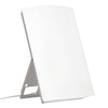 A white rectangular light therapy lamp with a thin frame, standing upright on a fold-out support with a power cord attached, provides bright LED illumination. Matte finish on front and frame; no visible logos or label text. No packaging shown. Plain background in neutral color, tabletop surface visible. No hands or people present. Standard product shot, straight-on angle.