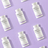 THERA Nordic Optimized Enzymes; valkoisia pulloja, joissa lukee "THERANORDIC Optimized Enzymes", on aseteltu vinoittain toistuvaan kuvioon vaaleanvioletilla taustalla, korostaen kehittynyttä entsyymikaavaa; pullot ovat sylinterinmuotoisia muovipulloja mattavalkoisella pinnalla ja valkoisin korkein; etiketin teksti on groteskia, kooltaan vaihtelevaa ja pääosin mustaa; kuvassa ei näy ihmisiä tai käsiä; tasakuva tasaisella valaistuksella.