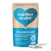 A blue and beige pouch of Together Health Magnesium supplements stands upright, labeled From Mineral Salts. Matte finish and flexible rectangular pouch with resealable top; front label uses mixed sans-serif fonts in white, light blue, and navy. Three off-white capsules rest on a plain white surface directly in front of the packaging. No people or hands are visible.