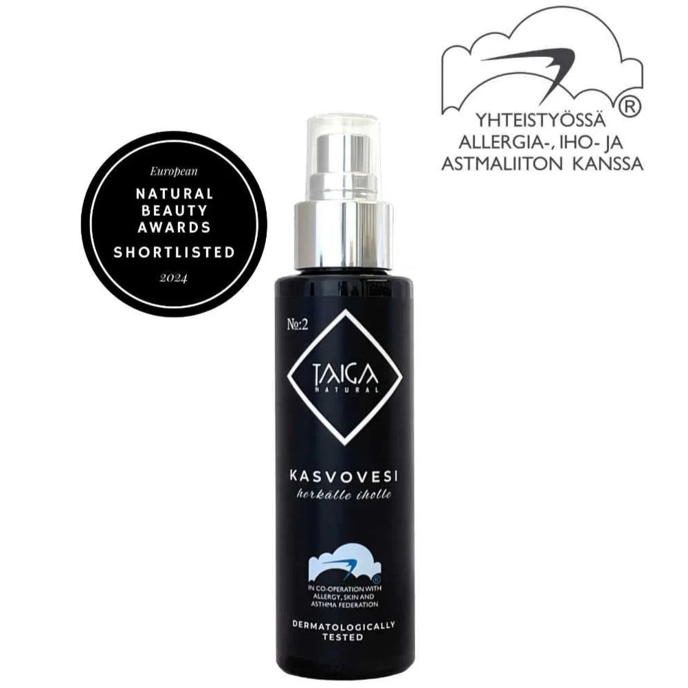 Taiga Cosmetics Kasvovesi; musta suihkepullo mattapinnalla, sylinterinmuotoinen ja pumppukorkillinen; etiketissä lukee "Taiga Natural Kasvovesi"; pakkauksessa palkintomerkki "Natural Beauty Awards Shortlisted 2024" sekä suomalaisen allergia-, iho- ja astmayhteistyön logo; ei ihmisiä tai käsiä näkyvissä; tausta yksivärinen tasaisesti valaistuna.