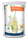 A packet of Water Kefir Starter Cultures, featuring an image of a mason jar filled with lemon, lime, mint, and a striped straw. Rectangular package with matte finish. Main colors are light blue and white. Clear branding from The Kefir Company is present at the top. Health icons appear in a row below the main image. Clean sans-serif typography dominates the front panel against a plain background. No people or hands visible in the shot.