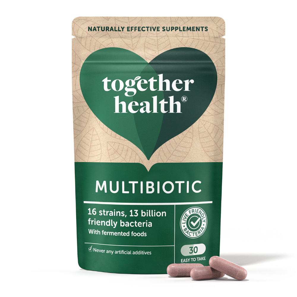 Vihreä ja beige pussi merkinnällä Together Health Multibiotic, kapseleita sen vierellä. Mattapintainen, joustava pakkaus pyöristetyin reunoin; luettavassa tekstissä mainitaan 16 kantaa, 13 miljardia bakteeria, fermentoituja ruokia ja probiootteja, sisältäen 30 kapselia. Pääteviivaton fontti valkoisella ja tummin värein. Pelkistetty tausta ilman näkyvää ympäristöä tai ihmisiä. Kuva on läheltä otettu tuotekuva.